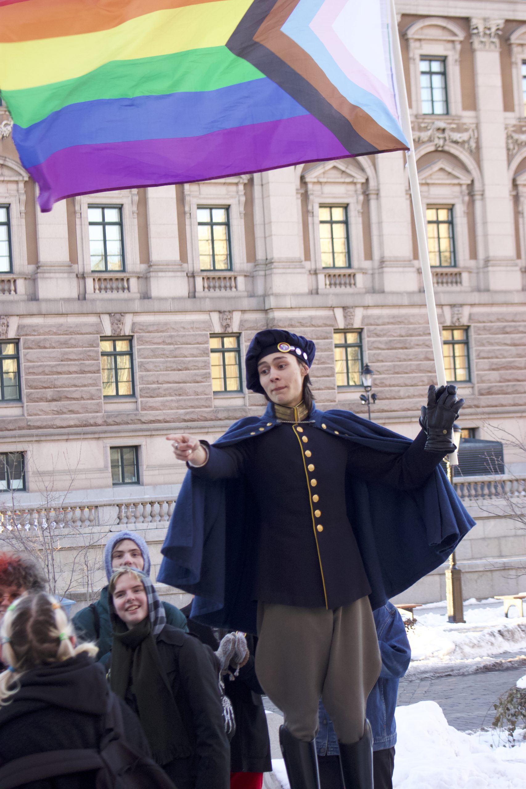 Photography of a person giving a speech and raising the progress pride flag.